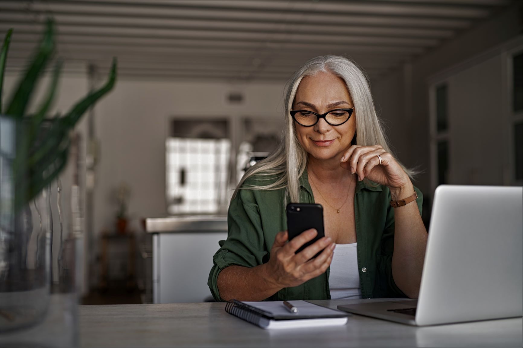 A woman looking at a mobile phone and a laptop.